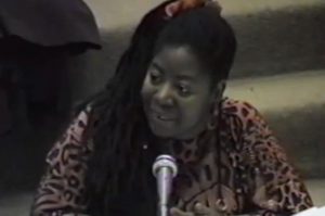 Still image of civil rights activist and public intellectual Loretta Ross speaking into a microphone at a seminar